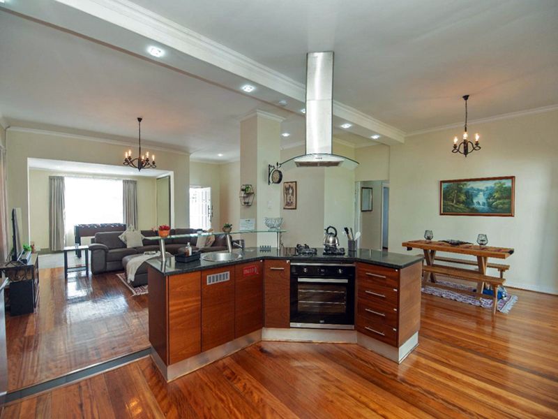 Spacious open-plan living area featuring a modern kitchen island with built-in oven, gas hob, and granite countertops, complemented by rich hardwood flooring throughout.