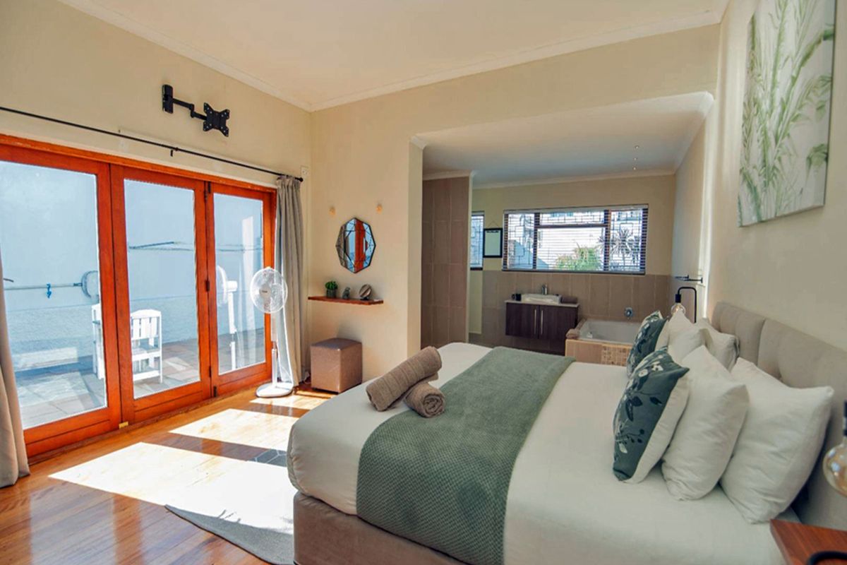 Spacious bedroom featuring hardwood flooring, wooden sliding doors leading to a patio, and an open-plan en-suite bathroom with a built-in vanity and bathtub.