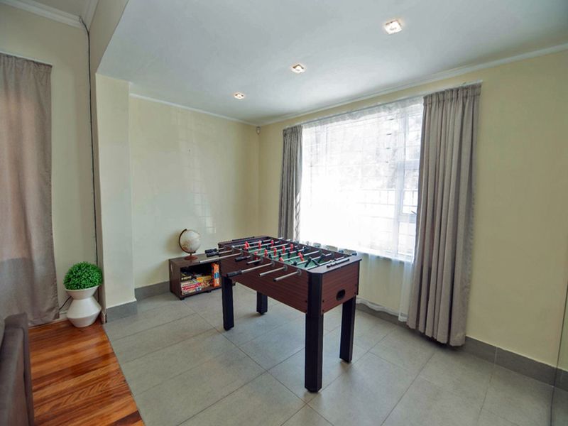A bright living area featuring a combination of tiled and wooden flooring, recessed ceiling lighting, and large windows with fitted curtain tracks.