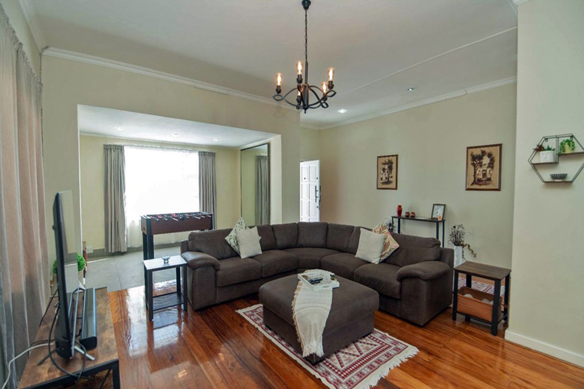 Spacious living room featuring polished hardwood flooring, elegant cove cornicing, and a classic wrought iron chandelier, creating a warm and inviting atmosphere.
