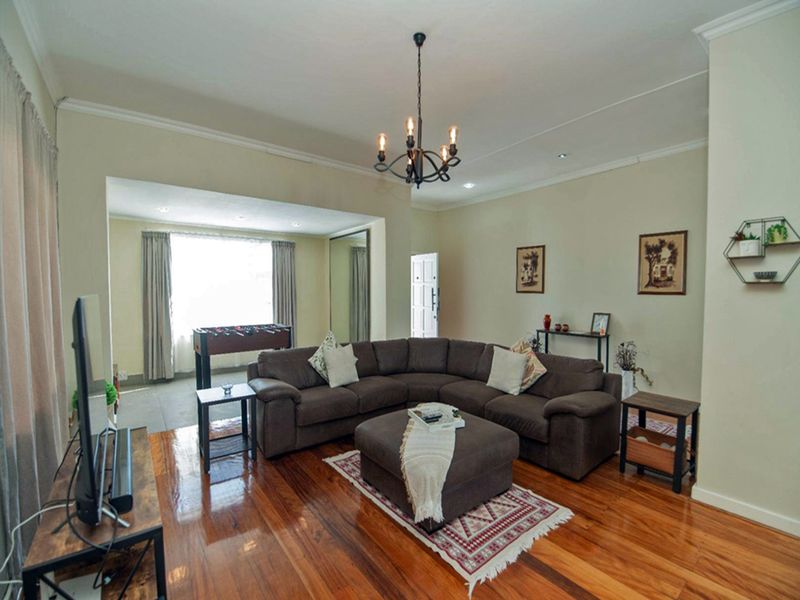 Spacious living room featuring polished hardwood flooring, elegant cove cornicing, and a classic wrought iron chandelier, creating a warm and inviting atmosphere.