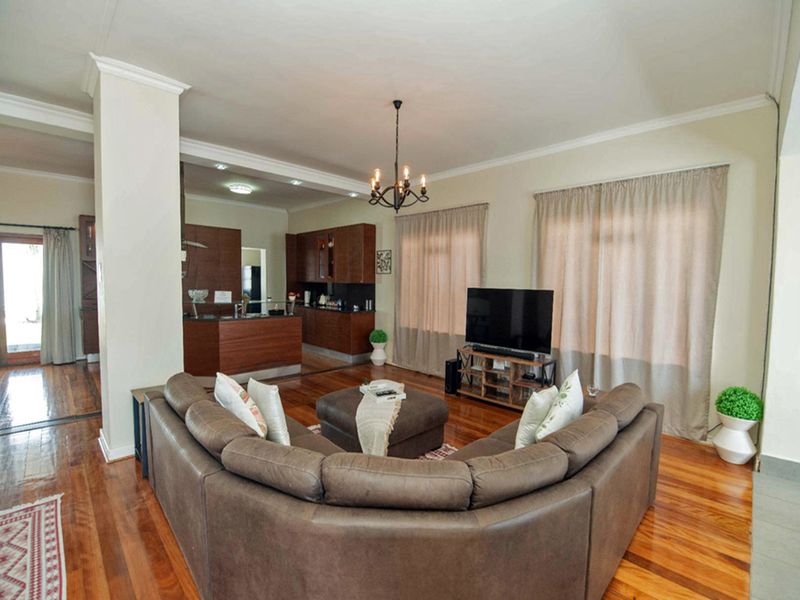 Spacious open-plan living area featuring polished hardwood floors, crown molding, and a seamless transition into a well-appointed kitchen with dark wood cabinetry.