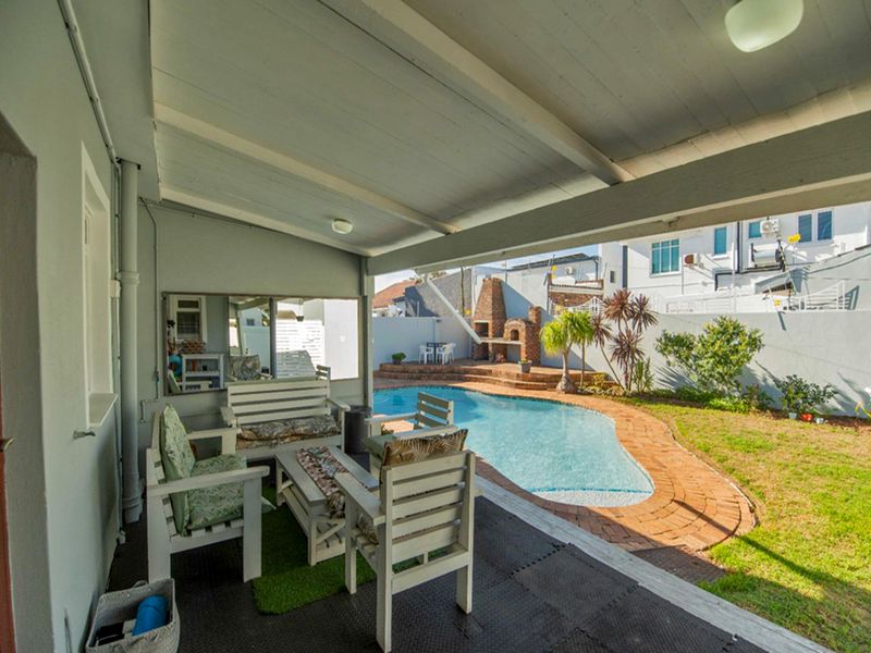 A covered patio area overlooking a swimming pool and a brick built-in braai, providing an ideal space for outdoor entertainment and relaxation.