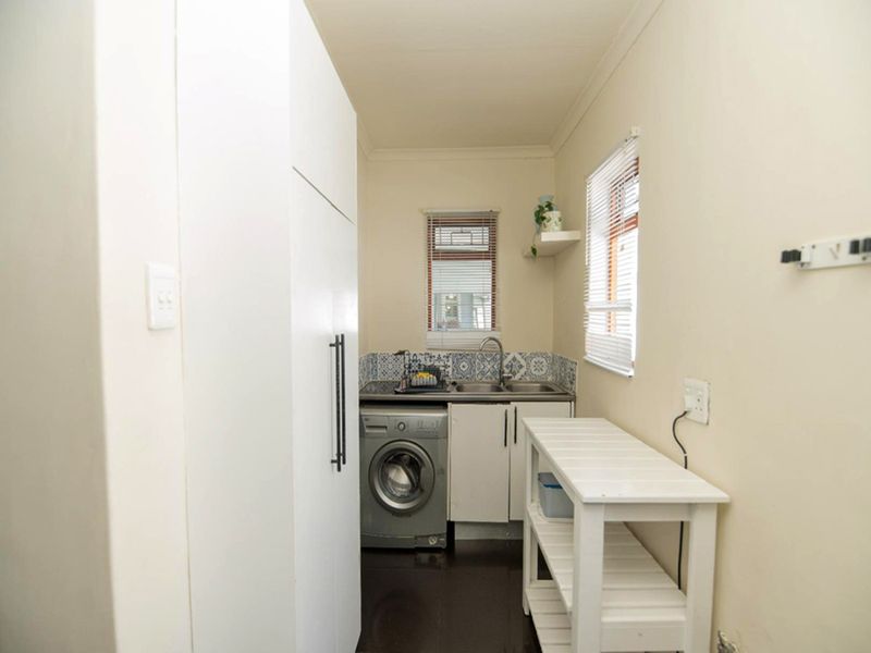 A functional laundry area featuring built-in cabinetry, a stainless steel sink, and a tiled backsplash, providing practical utility space.