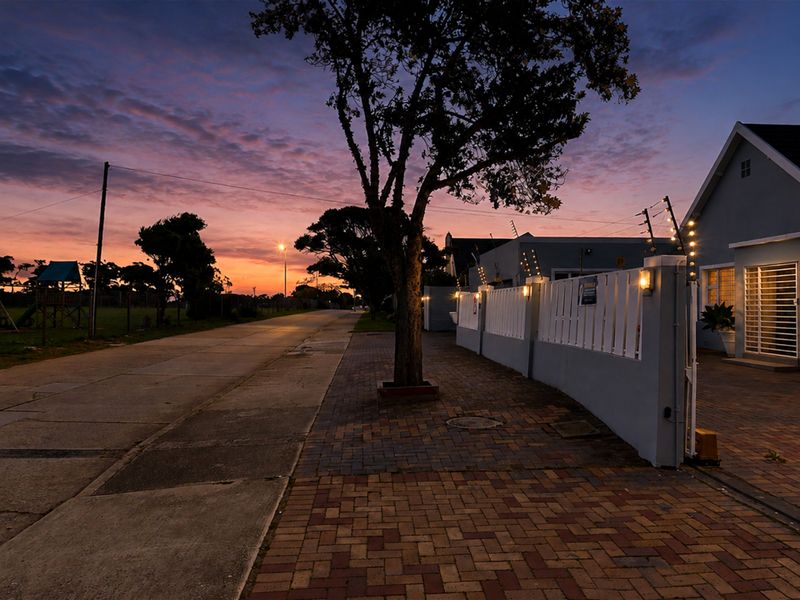 A twilight street view of the property featuring a paved driveway, secure boundary wall with electric fencing, and exterior lighting.