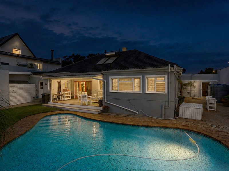 Rear exterior view featuring a swimming pool, paved patio area, and a well-maintained house facade with solar water heating installation.