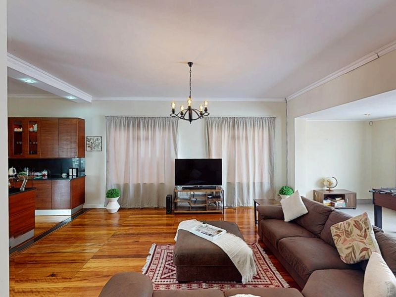 Spacious open-plan living area featuring polished hardwood flooring, crown molding, and an integrated kitchen with dark wood cabinetry.