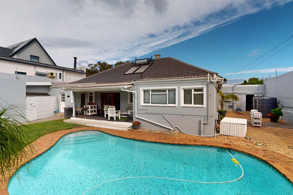 Rear exterior view featuring a swimming pool, paved patio area, solar water heating system, and enclosed garden space with boundary walls.