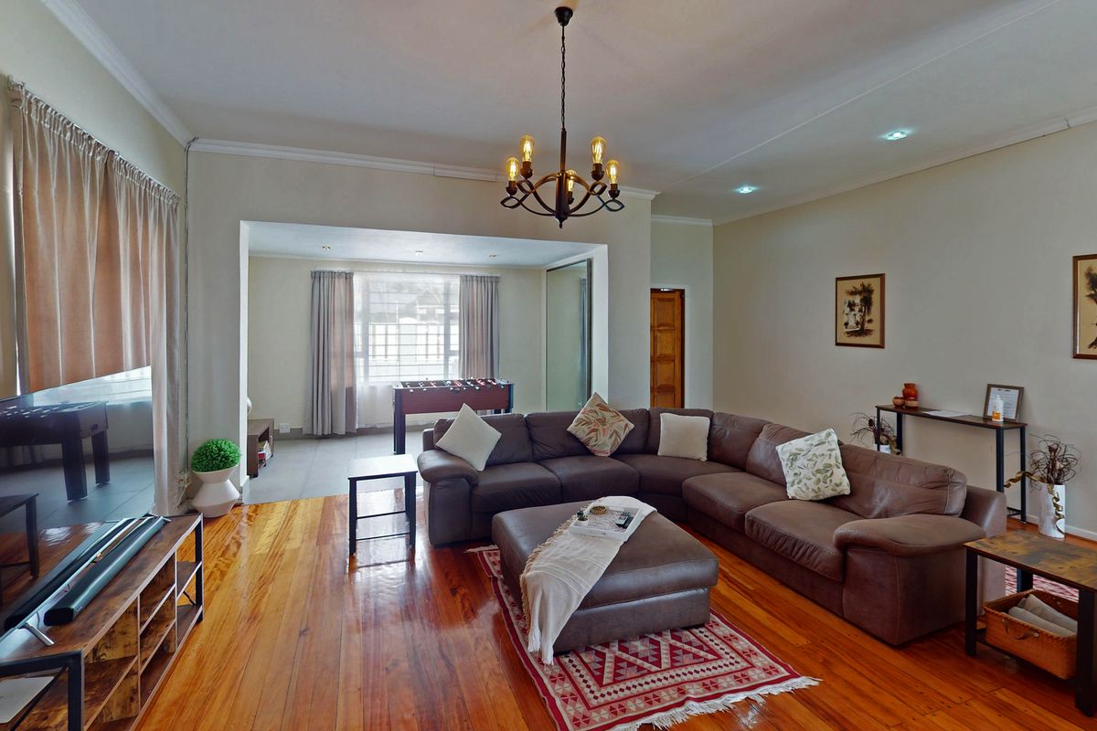 Spacious living room featuring polished hardwood flooring, recessed lighting, and a decorative chandelier, creating a warm and inviting atmosphere.