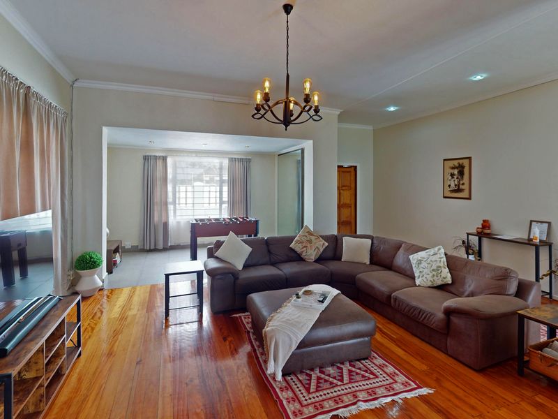 Spacious living room featuring polished hardwood flooring, recessed lighting, and a decorative chandelier, creating a warm and inviting atmosphere.