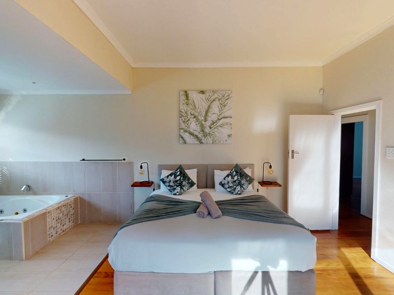 Spacious bedroom featuring an integrated en-suite bathtub, hardwood flooring, and neutral finishes, creating a comfortable and functional living space.