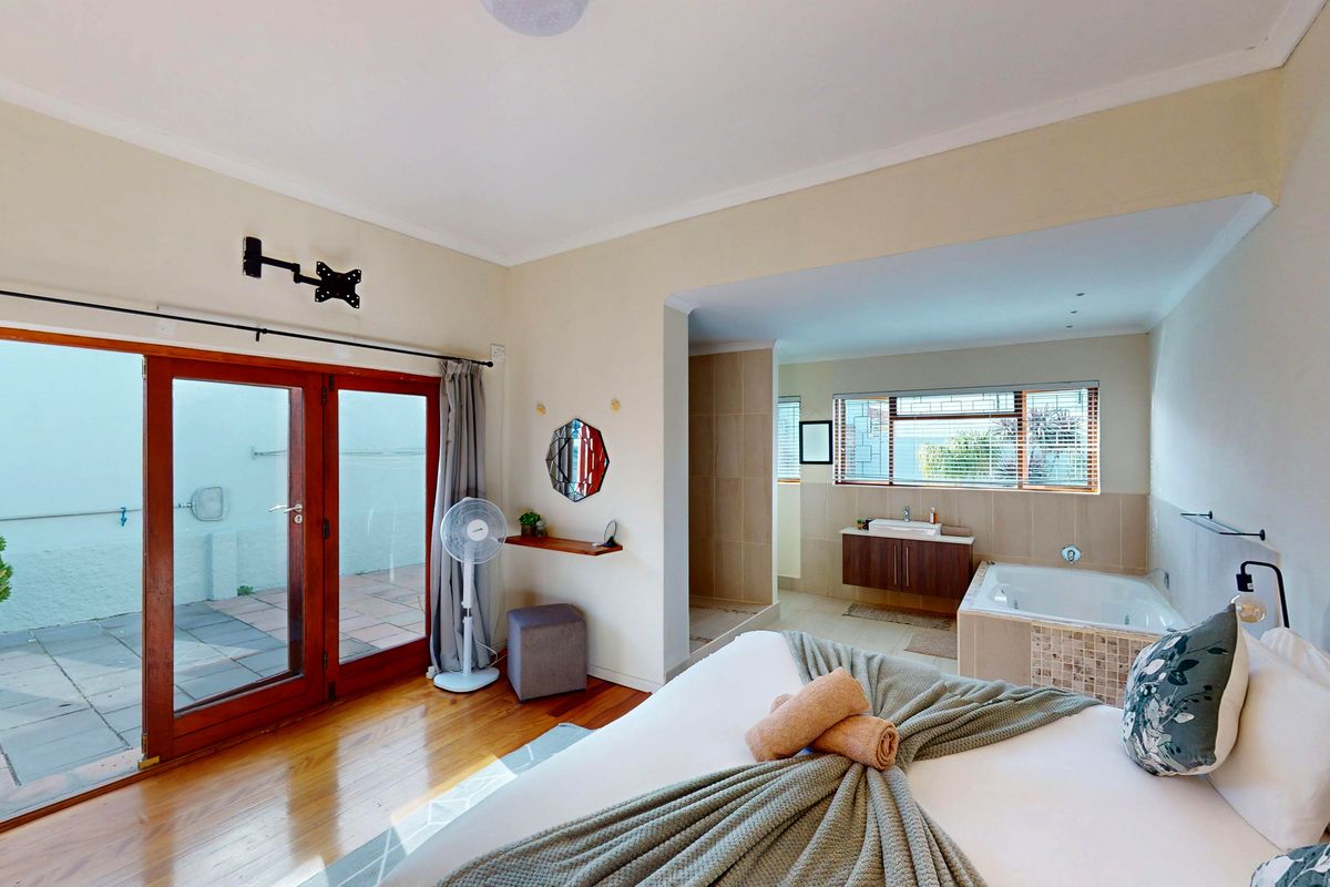 Spacious bedroom featuring hardwood floors, direct access to a private patio, and an open-plan en-suite bathroom with a built-in bathtub and vanity.