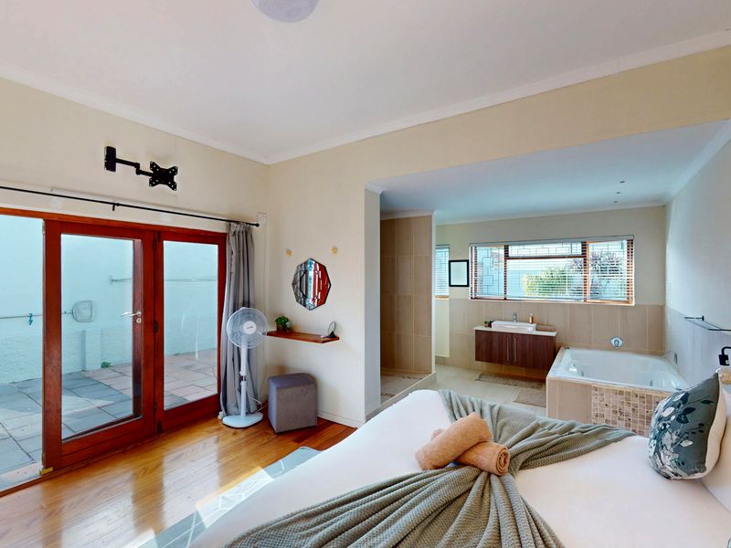 Spacious bedroom featuring hardwood floors, direct access to a private patio, and an open-plan en-suite bathroom with a built-in bathtub and vanity.