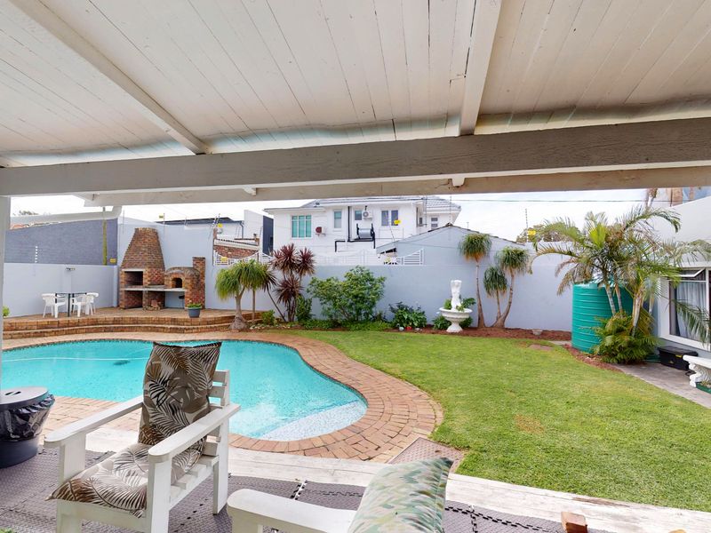 Outdoor entertainment area featuring a swimming pool, brick built-in braai, covered patio, and landscaped garden with boundary walls.