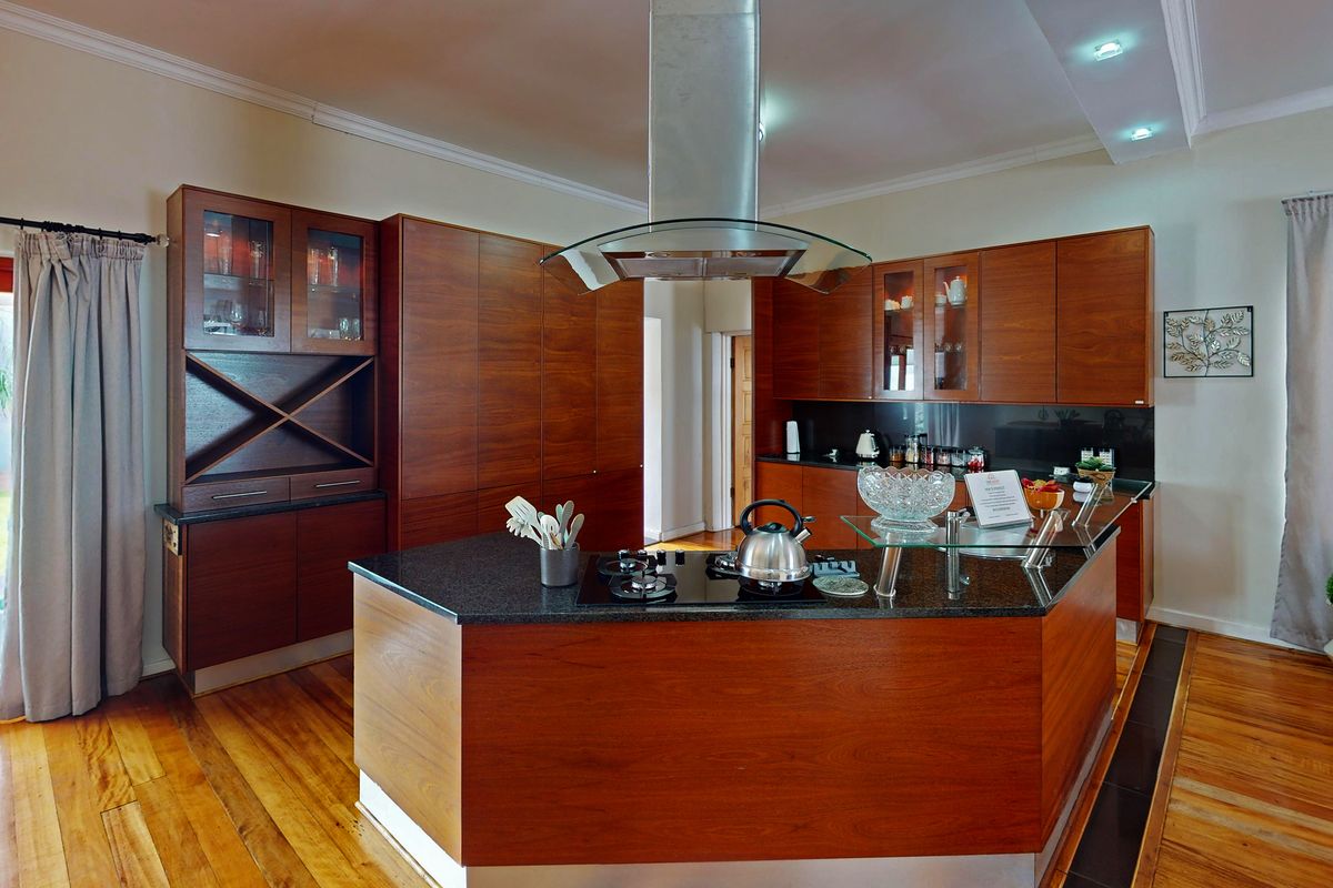 Modern kitchen featuring rich wooden cabinetry, granite countertops, a central island with a gas hob, and direct access to the rear garden.