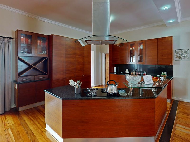 Modern kitchen featuring rich wooden cabinetry, granite countertops, a central island with a gas hob, and direct access to the rear garden.