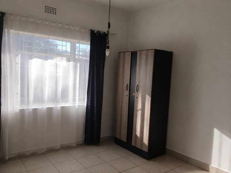 A bright, neutrally finished bedroom featuring tiled flooring and a large window, providing a clean and versatile space ready for personalization.