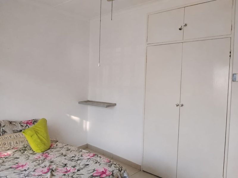 A bedroom featuring white built-in wardrobes with overhead storage, a wall-mounted shelf, and tiled flooring.