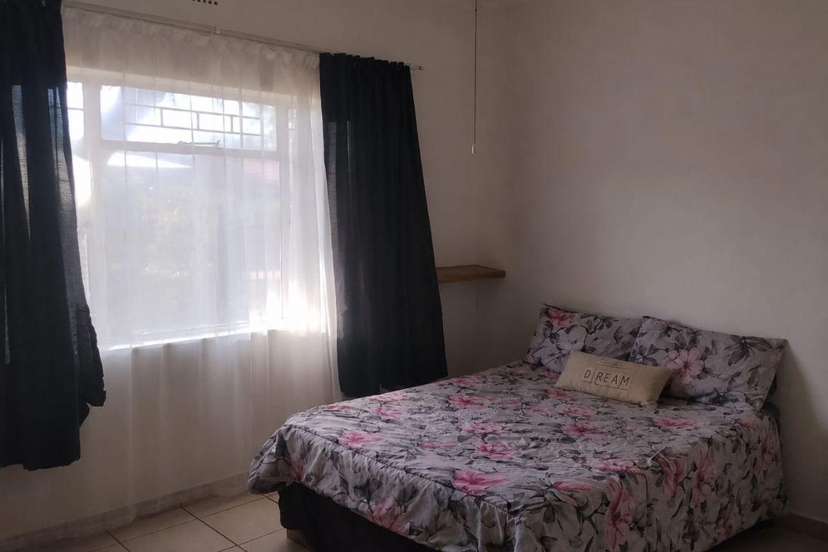 A simple bedroom featuring tiled flooring and a window with natural light, providing a functional space for rest.