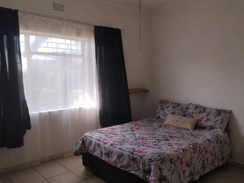A simple bedroom featuring tiled flooring and a window with natural light, providing a functional space for rest.