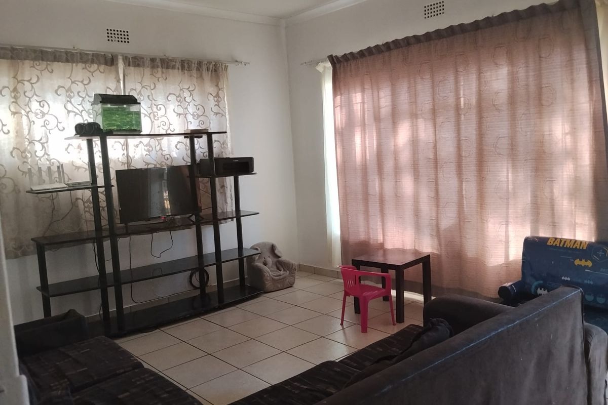 A living room featuring tiled flooring, neutral walls, and large windows with curtain treatments, providing a functional and well-lit living space.
