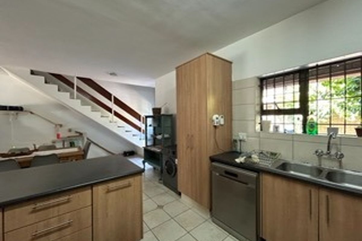 Open plan kitchen area featuring laminate cabinetry, double basin sink, and tiled flooring, adjacent to a staircase with a wooden handrail.