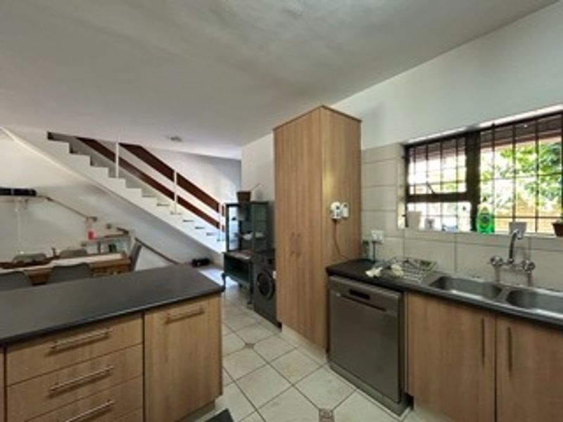 Open plan kitchen area featuring laminate cabinetry, double basin sink, and tiled flooring, adjacent to a staircase with a wooden handrail.
