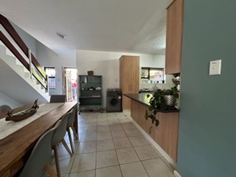Open plan living and kitchen area featuring tiled flooring, wooden cabinetry, a breakfast bar, and an internal staircase leading to the upper level.