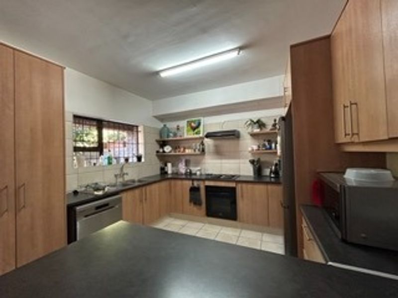 A functional kitchen featuring wood-finish cabinetry, dark countertops, built-in oven and hob, and tiled flooring with ample storage space.