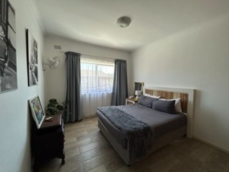 A well-maintained bedroom featuring tiled flooring, a wall-mounted fan, and neutral finishes, providing a comfortable and functional living space.
