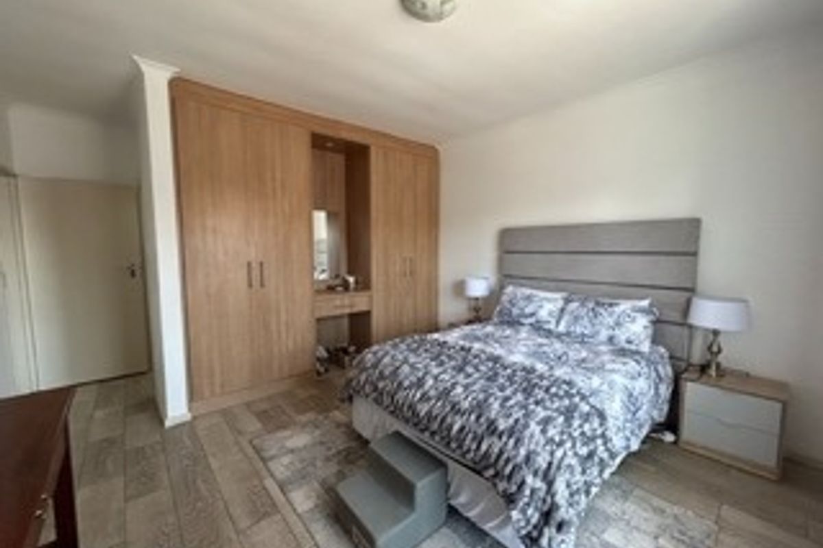 A well-maintained bedroom featuring extensive built-in wooden cupboards with an integrated vanity station and durable tiled flooring.