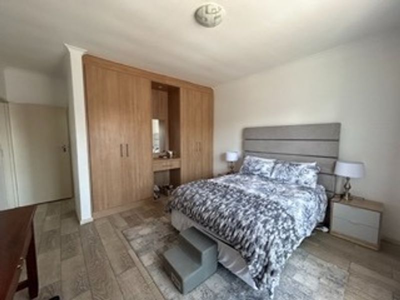 A well-maintained bedroom featuring extensive built-in wooden cupboards with an integrated vanity station and durable tiled flooring.