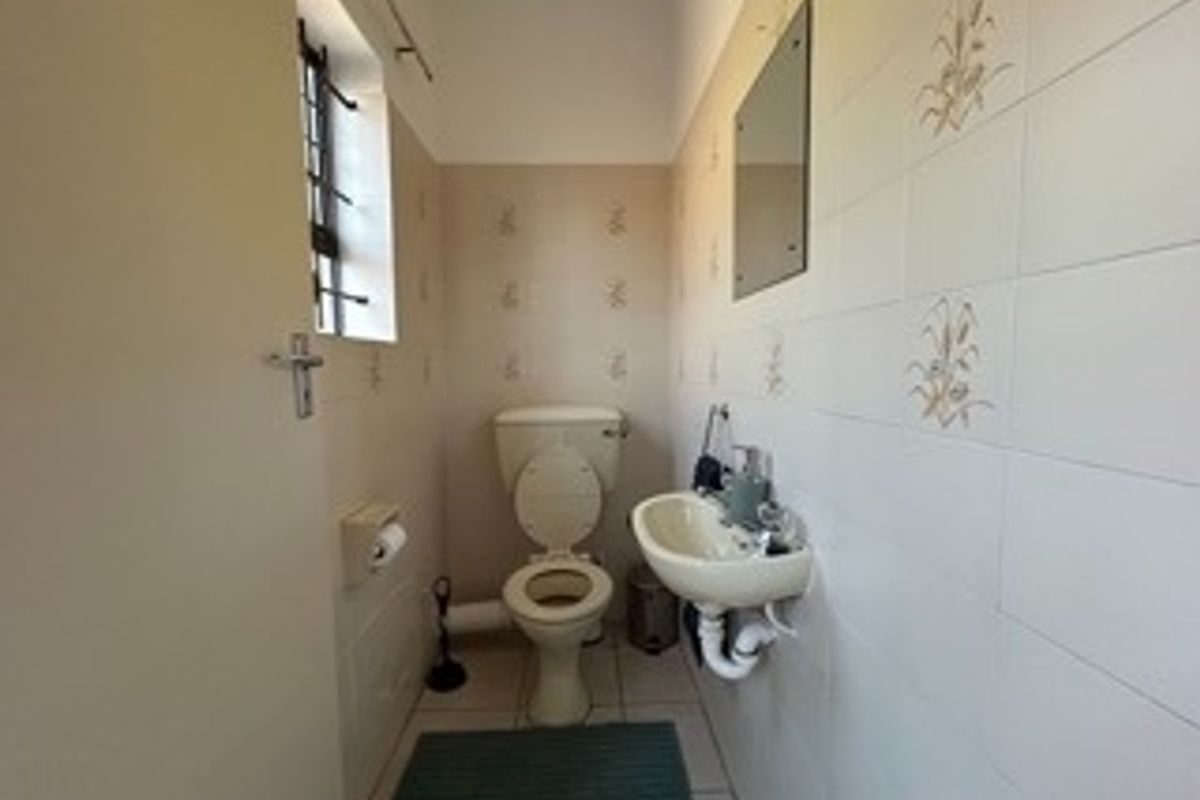 A compact guest bathroom featuring a wall-mounted basin, toilet, and neutral tiled walls with decorative accents.