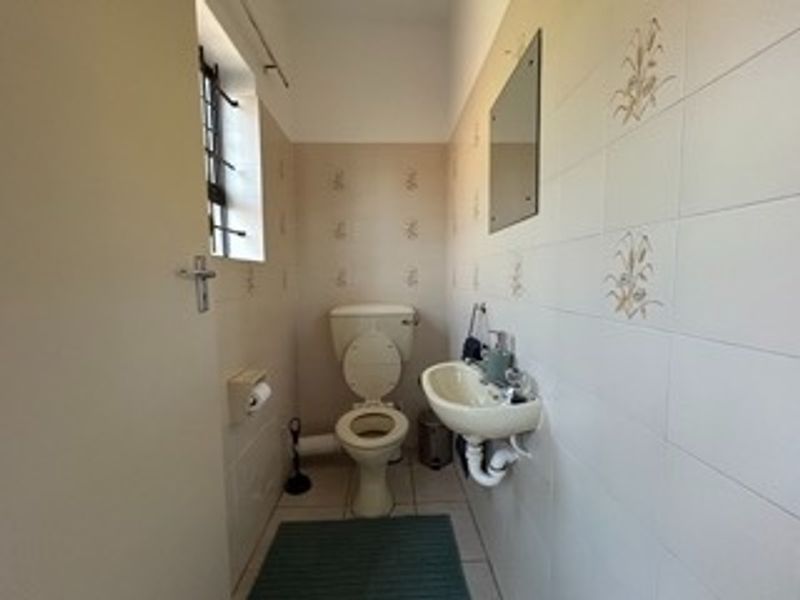 A compact guest bathroom featuring a wall-mounted basin, toilet, and neutral tiled walls with decorative accents.