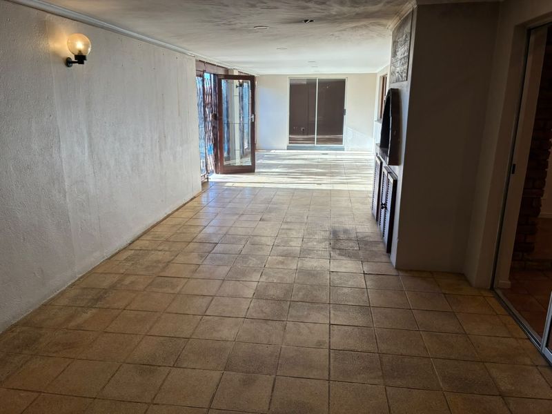 A spacious, empty covered patio featuring tiled flooring, a built-in braai, and sliding door access to the exterior.