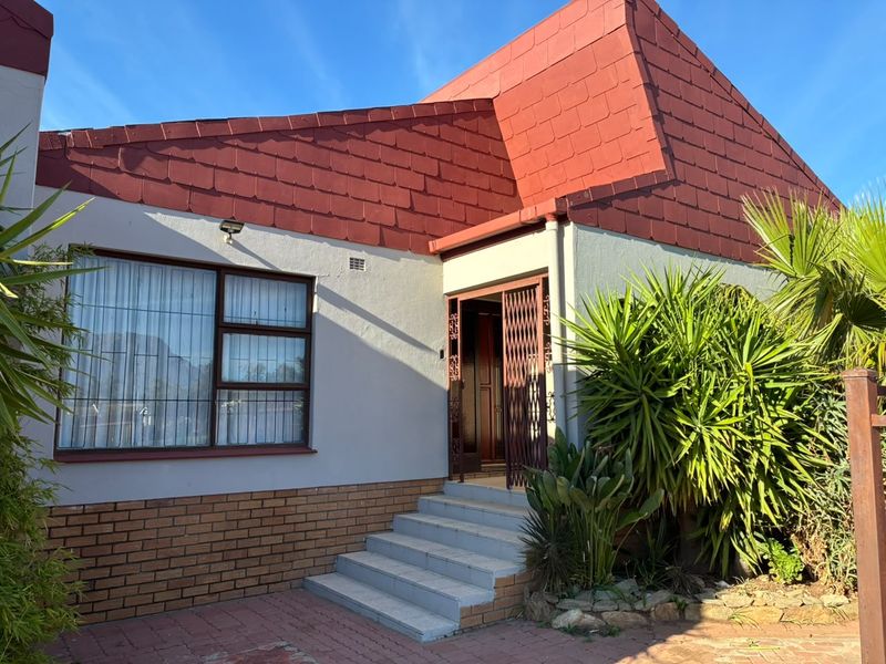 Front elevation of a house featuring a tiled roof, brick base, and secure entrance with security gate and window bars.