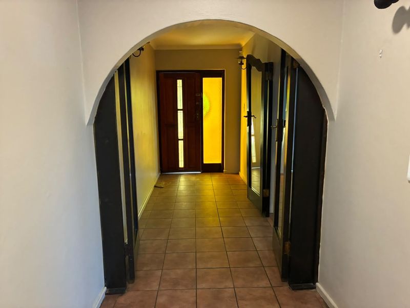 An entry hallway featuring an arched transition, tiled flooring, and a timber front door with a sidelight window.