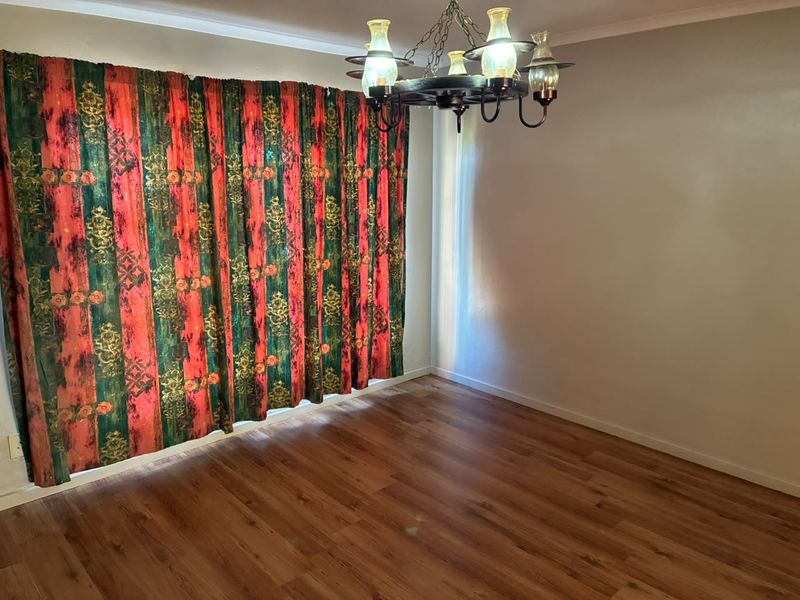 An empty living room featuring laminate wood flooring, a decorative chandelier, and floor-to-ceiling curtains.