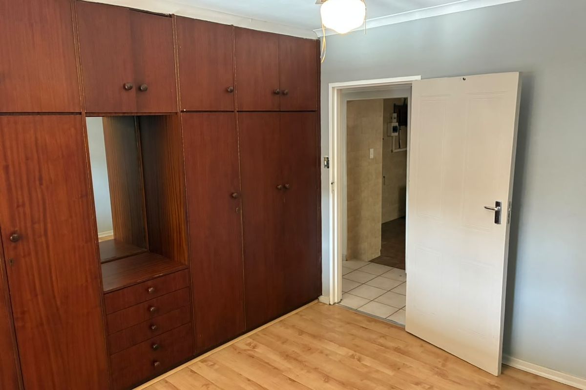 A bedroom featuring extensive built-in wooden cupboards, laminate flooring, and a ceiling fan, with direct access to an adjacent tiled room.