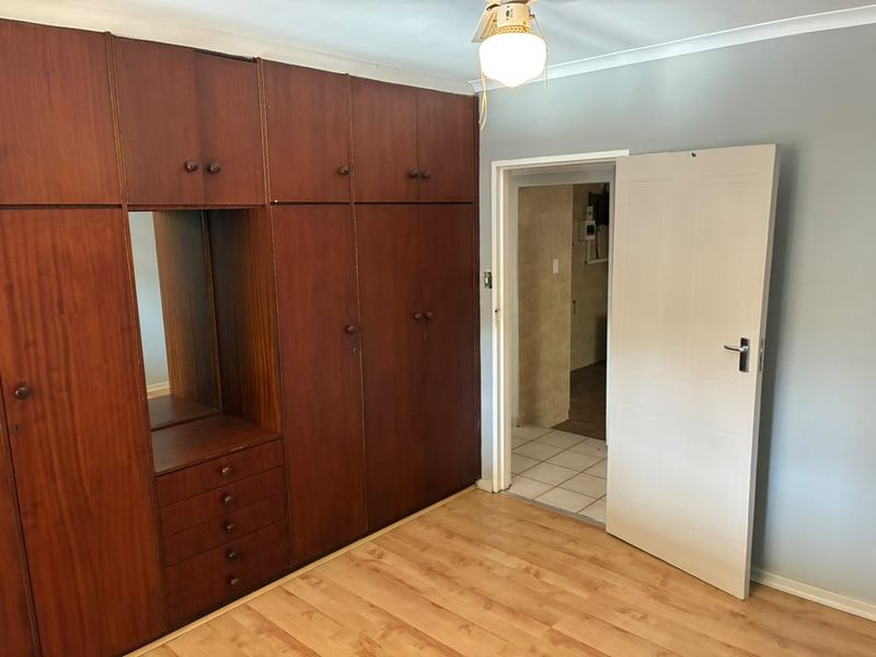 A bedroom featuring extensive built-in wooden cupboards, laminate flooring, and a ceiling fan, with direct access to an adjacent tiled room.