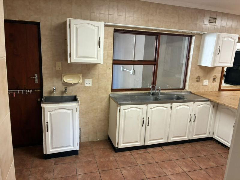 A functional scullery area featuring double stainless steel sinks, a separate utility sink, white cabinetry, and tiled finishes throughout.