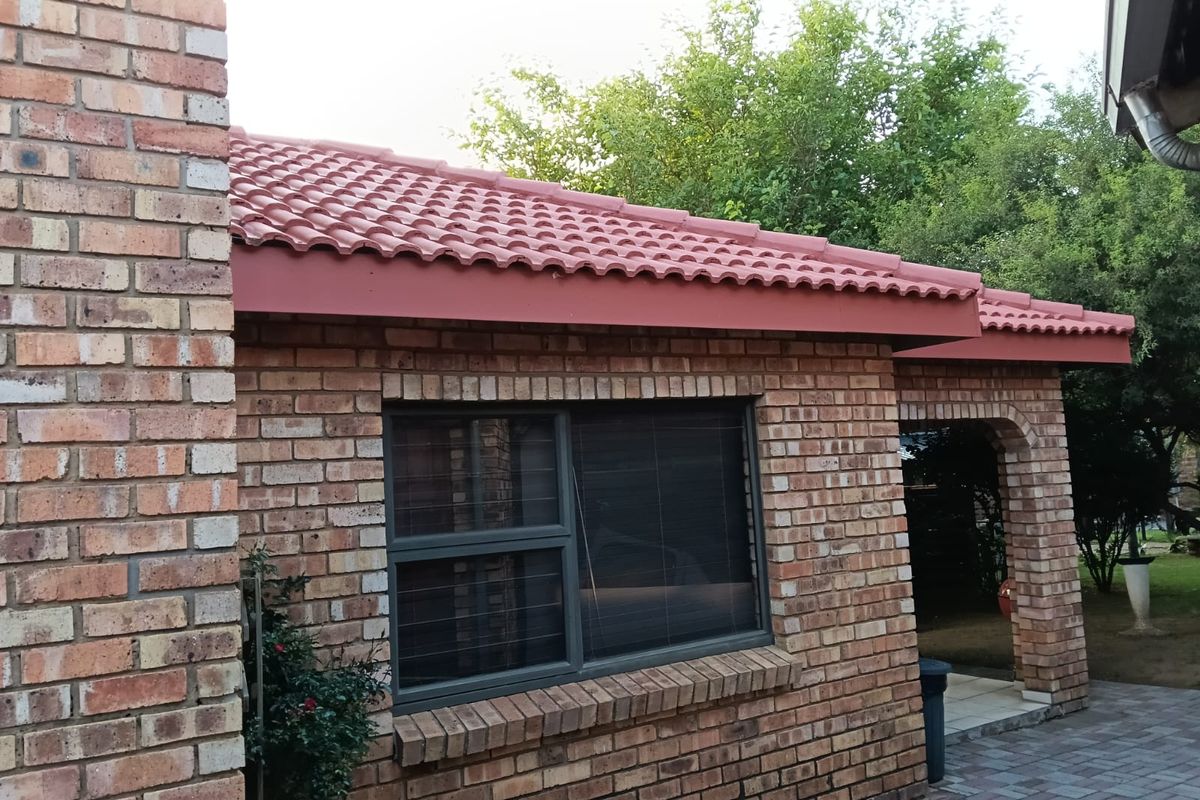 A view of the rear exterior featuring face brick walls, terracotta roof tiles, and a paved patio area with aluminium window frames.