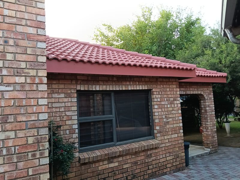 A view of the rear exterior featuring face brick walls, terracotta roof tiles, and a paved patio area with aluminium window frames.