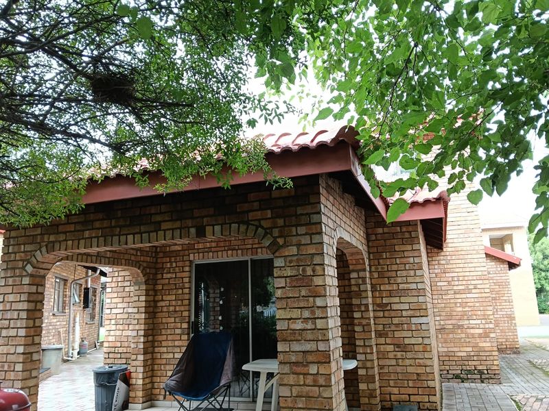 A covered patio area featuring face brick construction, arched columns, and a tiled roof, providing a sheltered outdoor space with direct access to the home.