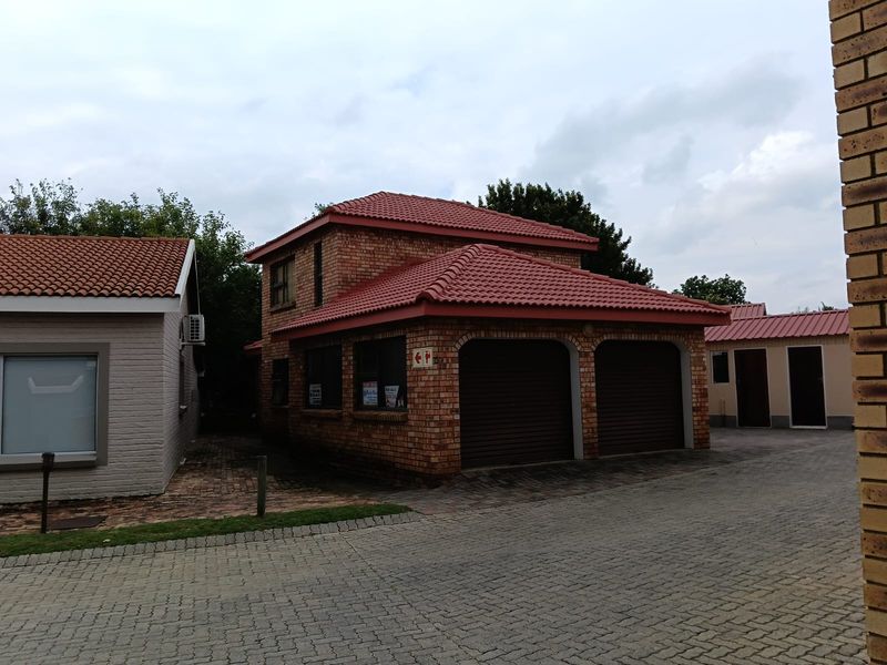 A double-story brick house featuring a double garage with roller doors and a tiled roof, situated on a paved driveway.