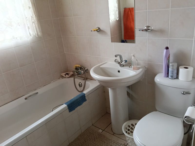 A functional bathroom featuring a pedestal basin, bathtub with mixer tap, and full wall tiling. The space is well-maintained but dated in style.