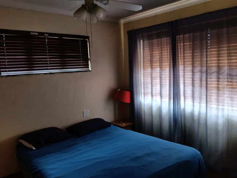 A bedroom featuring a ceiling fan, venetian blinds, and curtain tracks, with neutral wall tones and natural light filtering through the window treatments.