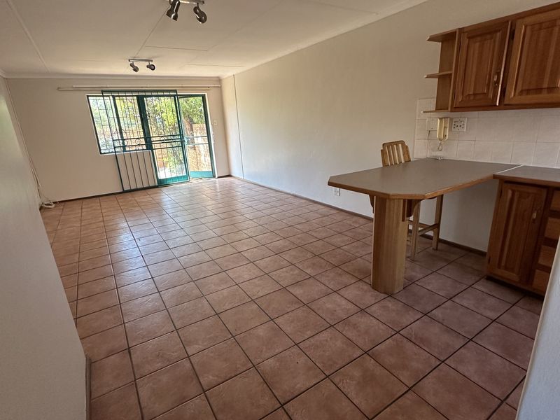 Open-plan living and kitchen area featuring tiled flooring, built-in wooden cabinetry, a breakfast counter, and a sliding door leading to the exterior.