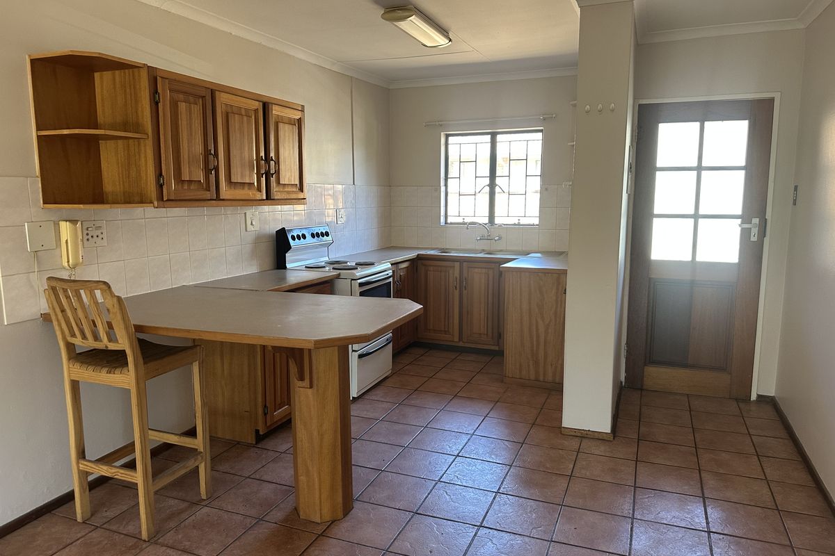 A functional kitchen featuring wooden cabinetry, tiled flooring, a freestanding stove, and a built-in breakfast counter with direct access to an exterior door.