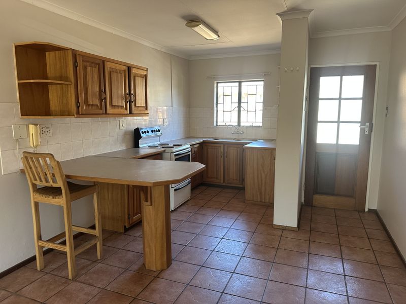 A functional kitchen featuring wooden cabinetry, tiled flooring, a freestanding stove, and a built-in breakfast counter with direct access to an exterior door.